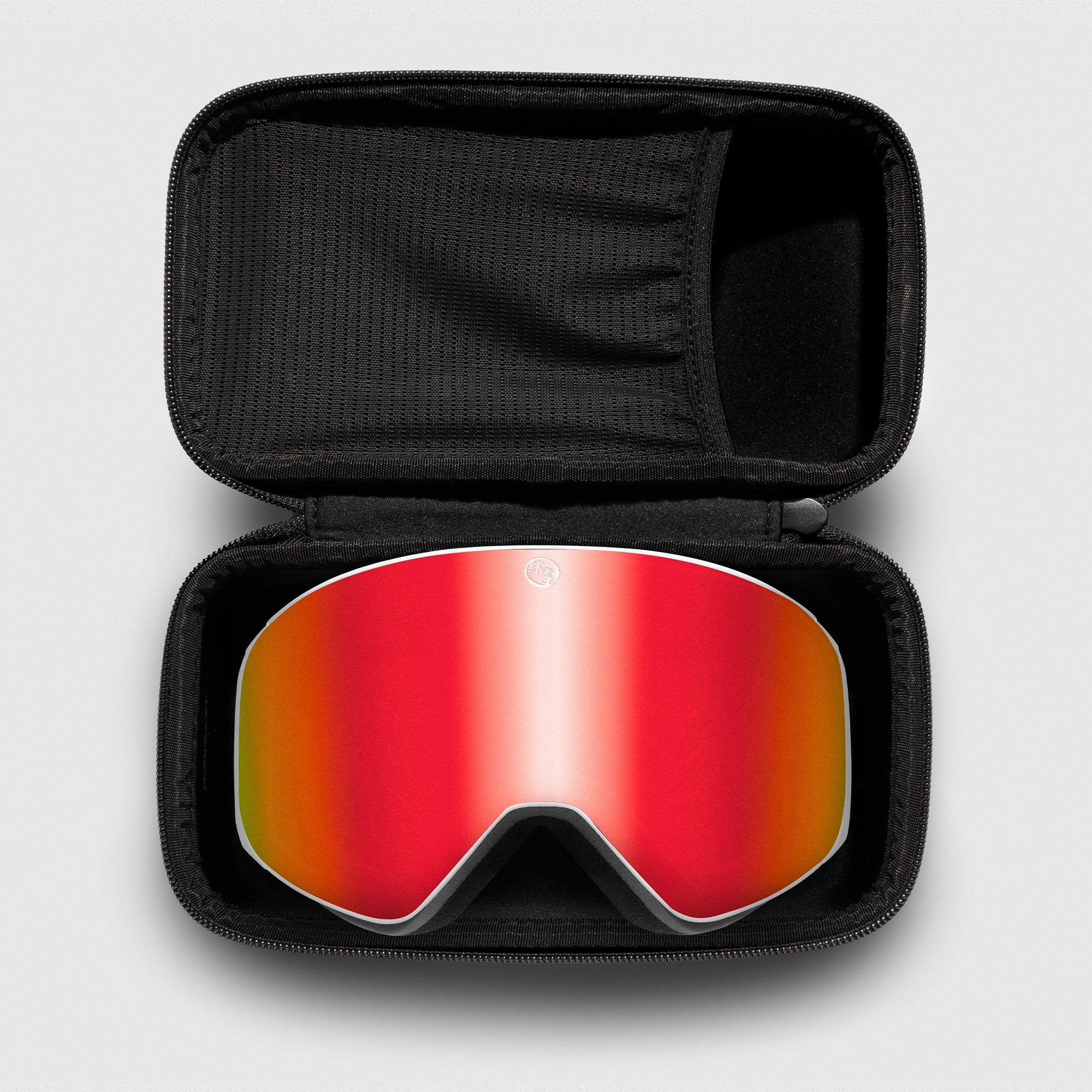 Red reflective ski goggles, with white frame in a black case on a light gray background