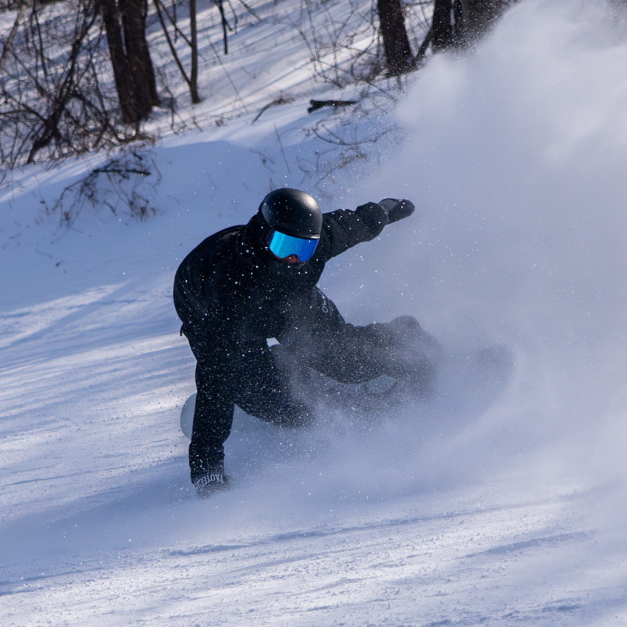 Person snowboarding through powder snow in a snowy landscape with trees.