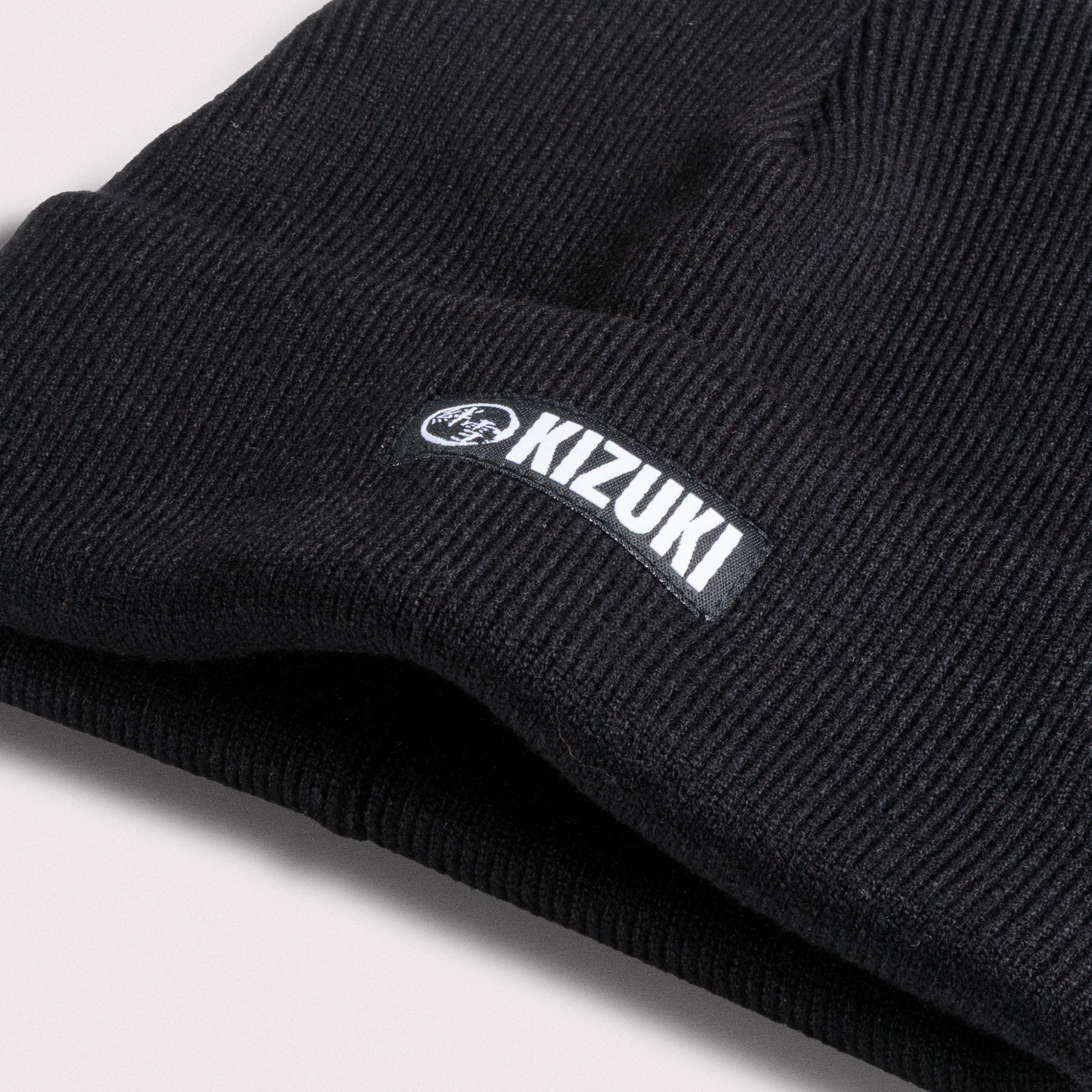 Close up shot of a Black beanie with Kizuki logo on a light gray background