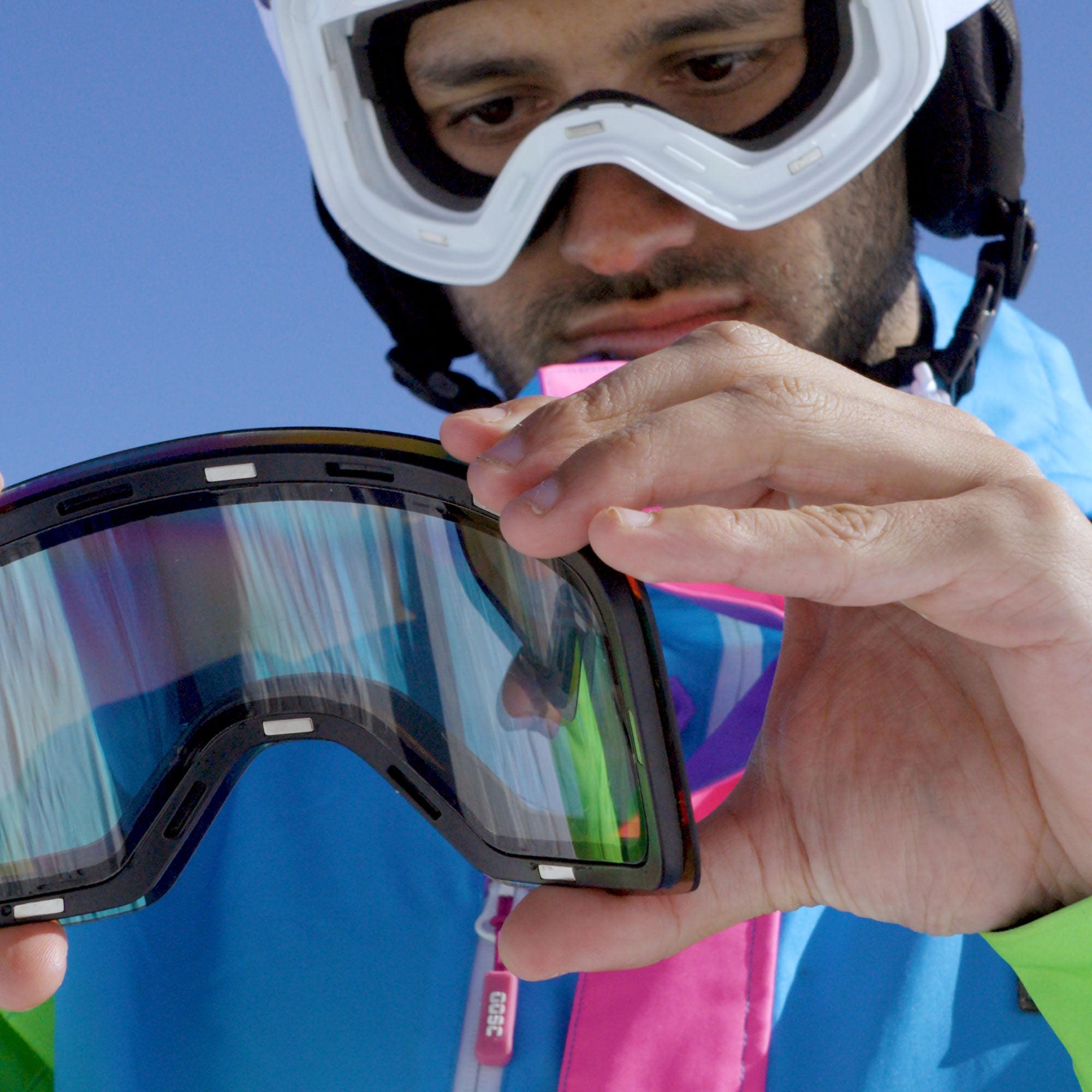Person holding a colorful ski goggles with a blue sky background