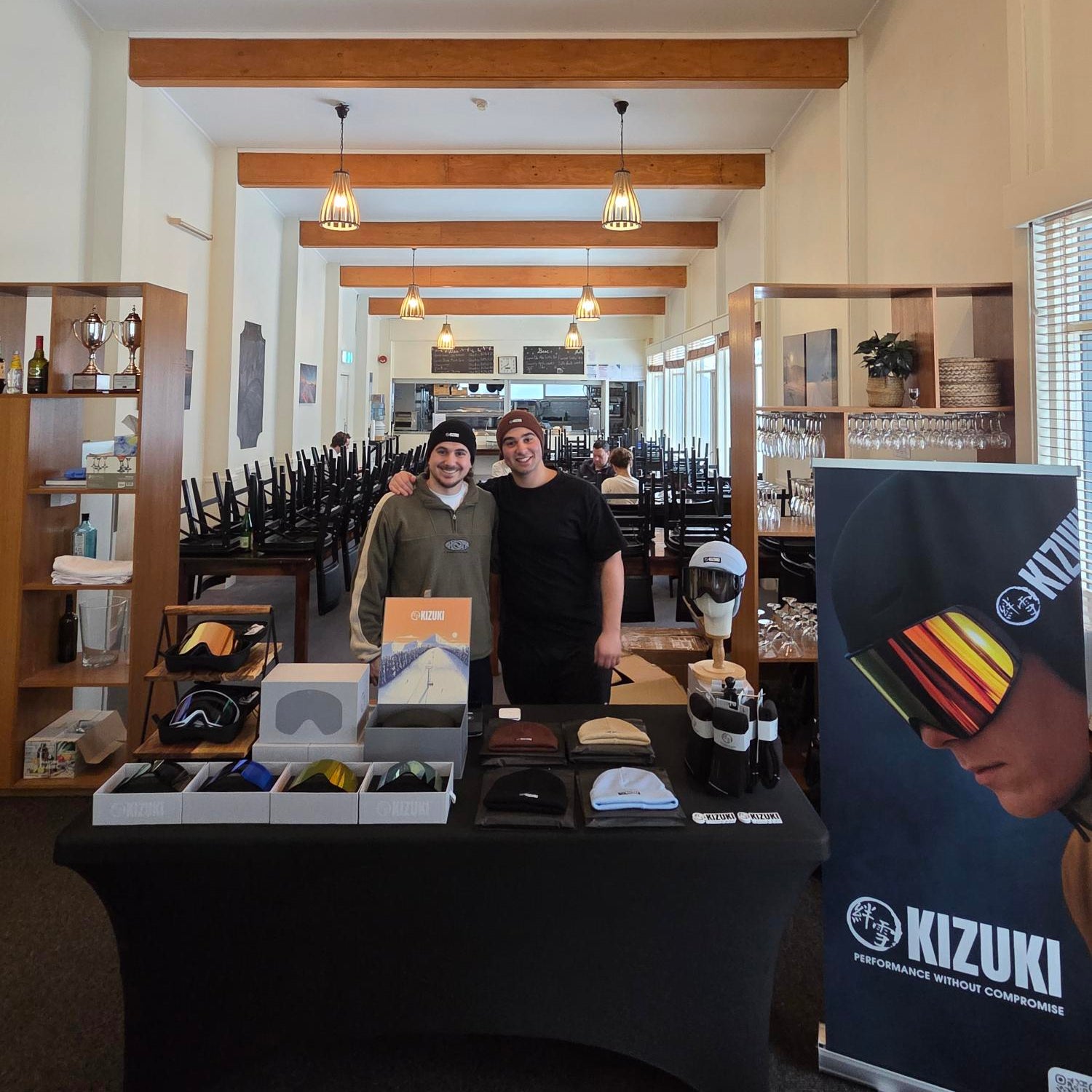 Two people standing behind a counter in a store with various items on display, including a Kizuki banner.