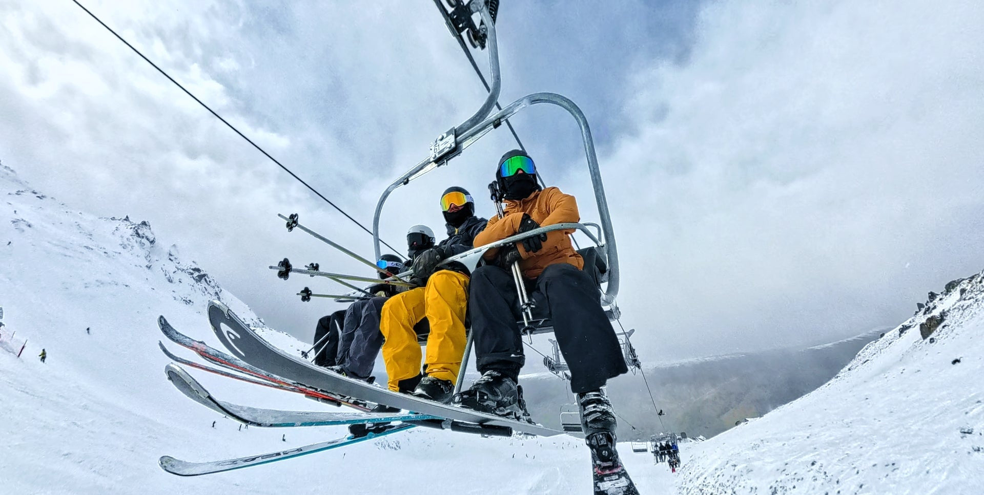 People on a ski lift with skis attached, surrounded by snow-covered mountains.