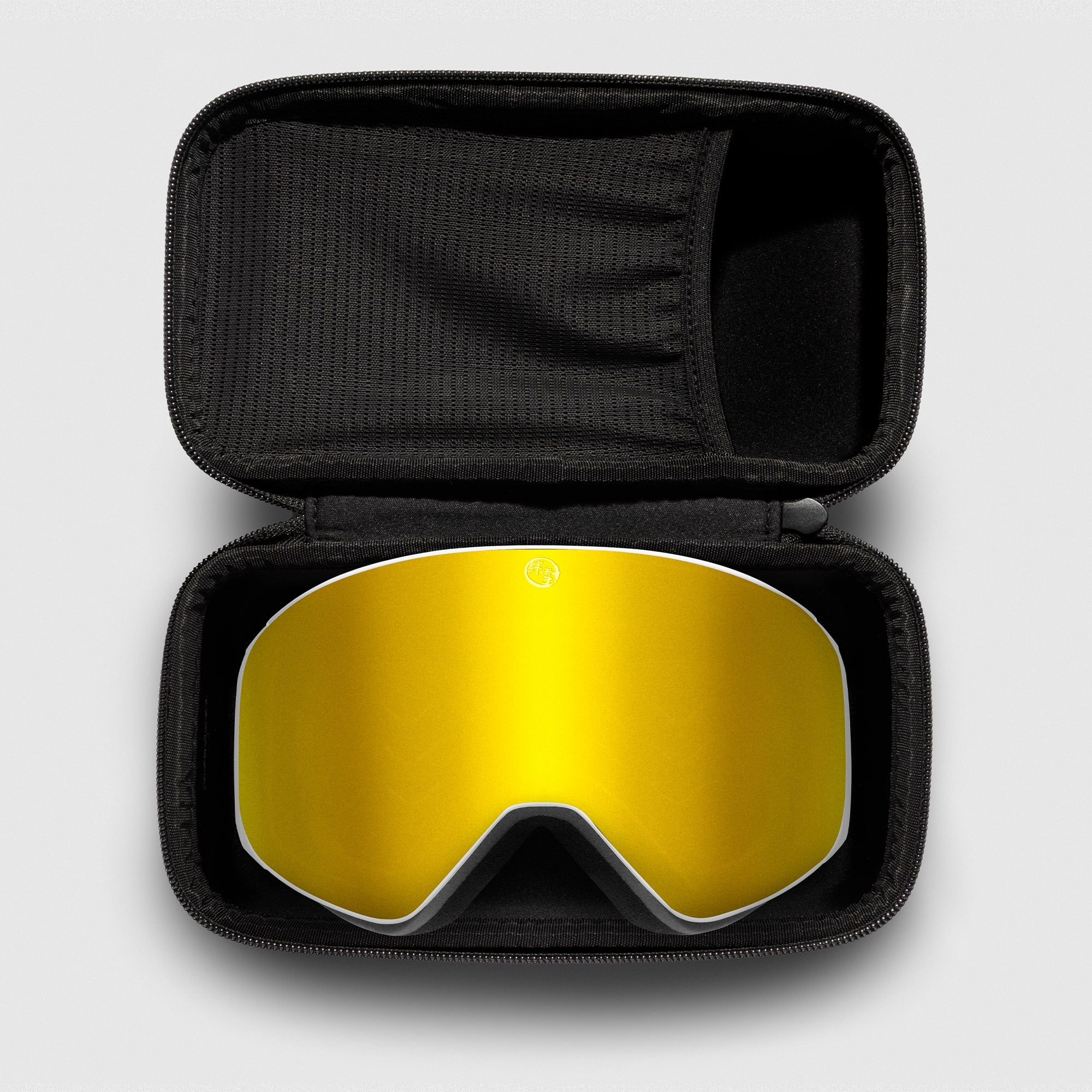 Gold reflective ski goggles, with white frame in a black case on a light gray background