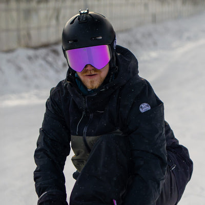 Man wearing KIZUKI Dawn ski goggles with Alpine Pink lens and black helmet on snowy slopes.