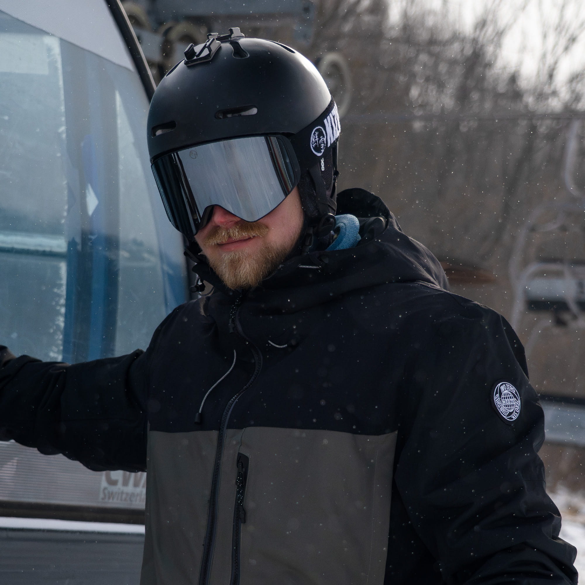Man wearing KIZUKI Dawn ski goggles with Blizzard Silver lens and black helmet outdoors in snow.