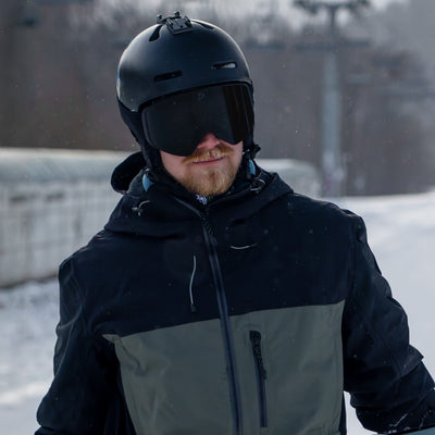 Man wearing KIZUKI Dawn ski goggles with Midnight Black lens and black helmet in alpine setting.