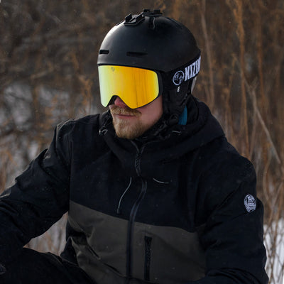 Man wearing KIZUKI Dawn ski goggles with Summit Gold lens and black helmet in snowy conditions.