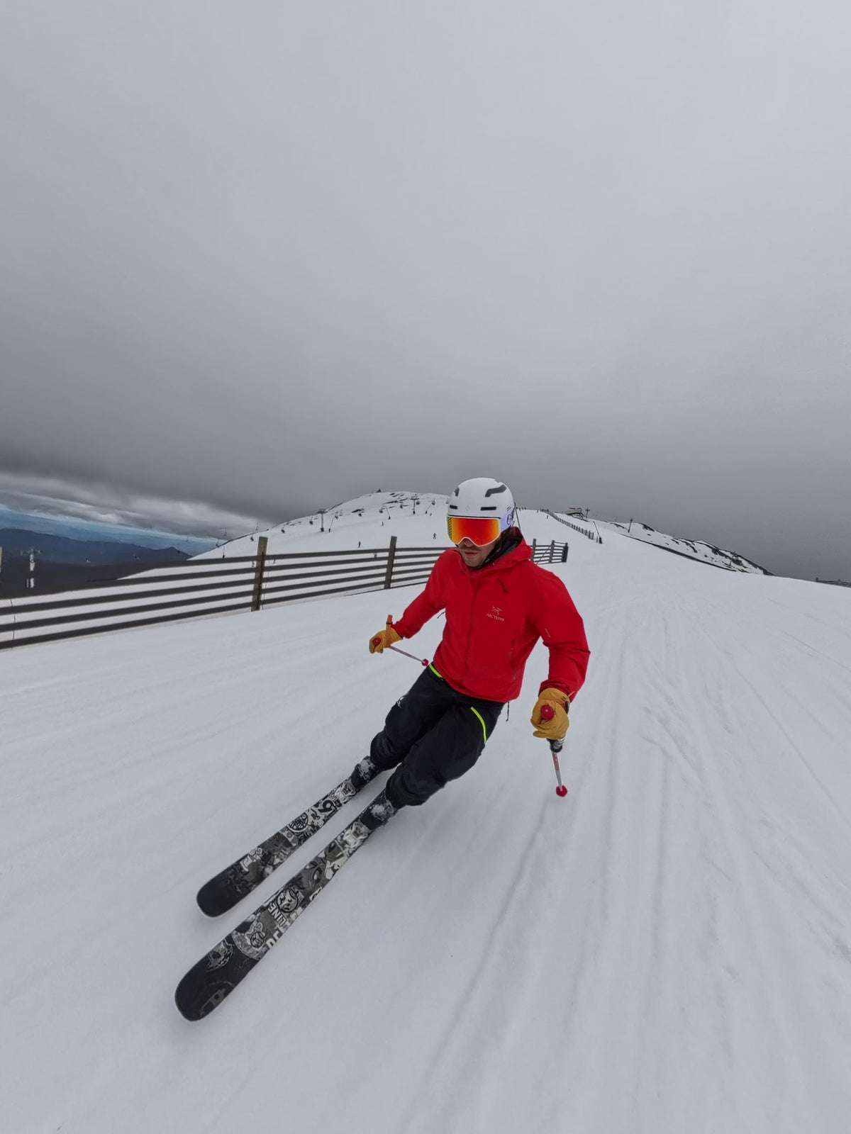 Load video: Skier in a red jacket carving down a snowy slope while wearing mirrored ski goggles in overcast alpine conditions